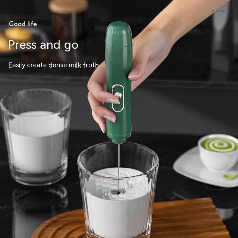 A hand frothing milk in a glass with the green Fourfold Froth 3