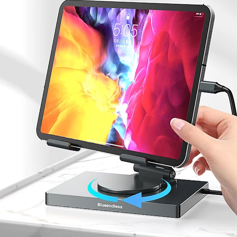 A hand turning a tablet round on the Fourfold 360 Tablet Stand & Hub's turntable base, a USB-C cable plugged into the back
