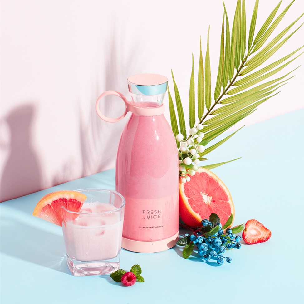 Fourfold Whirl 350 pink portable blender standing beside a glass of smoothie, grapefruit and a palm leaf